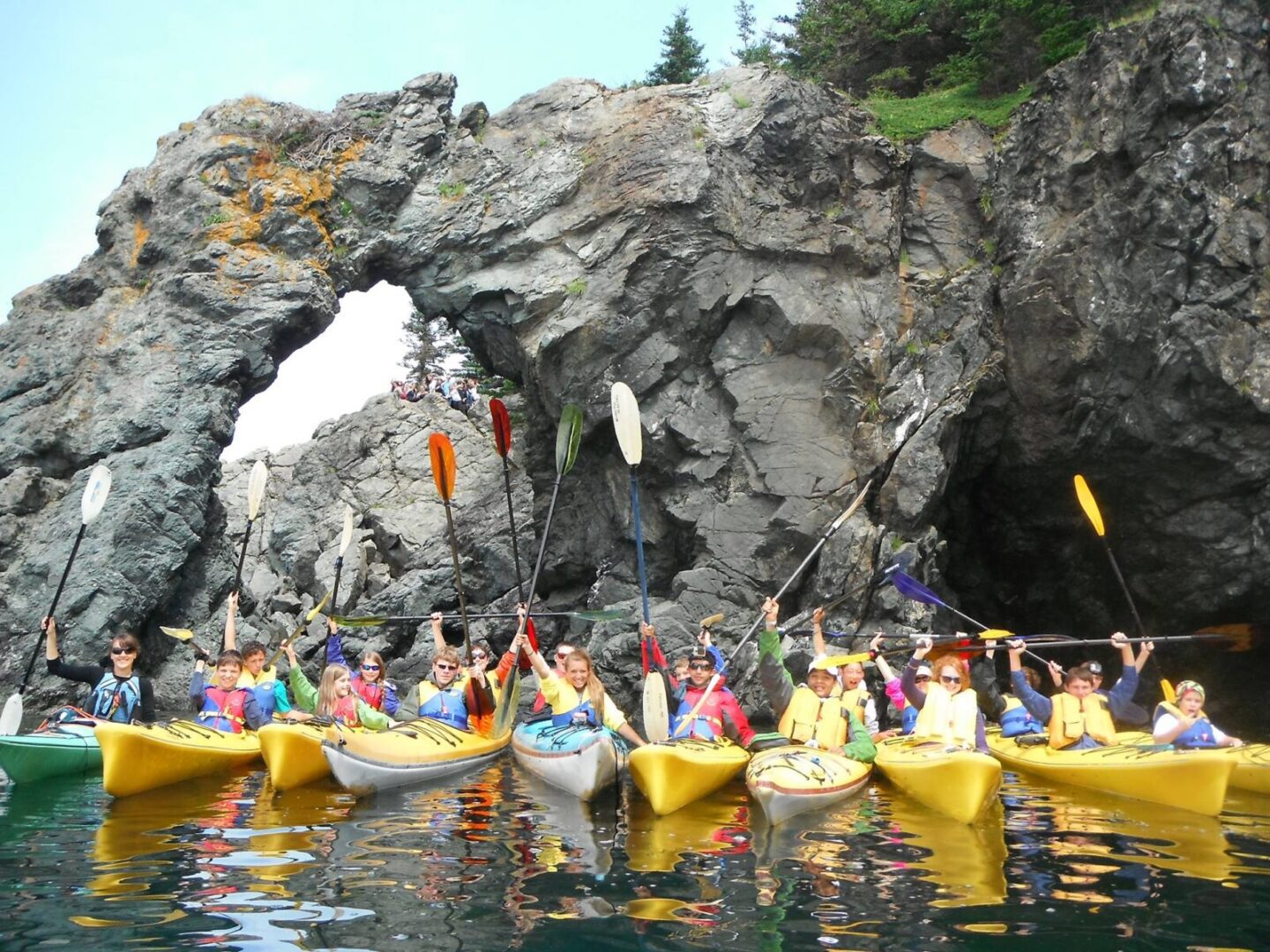 A group of people in kayaks in front of a rock formation.