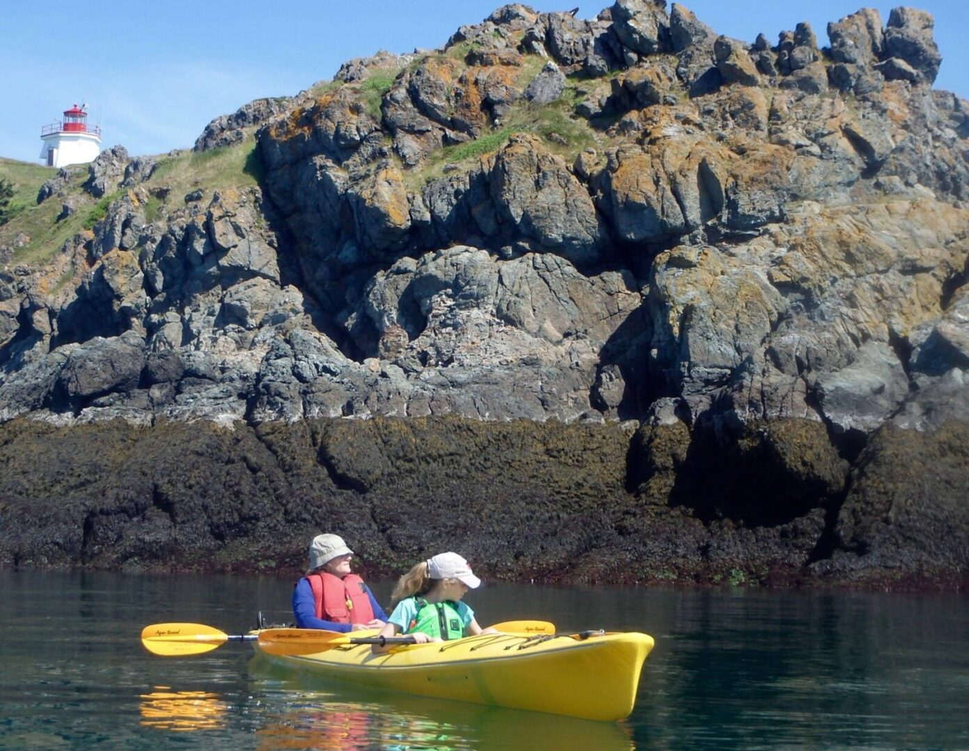 Two people paddling a yellow kayak in the water near a lighthouse.