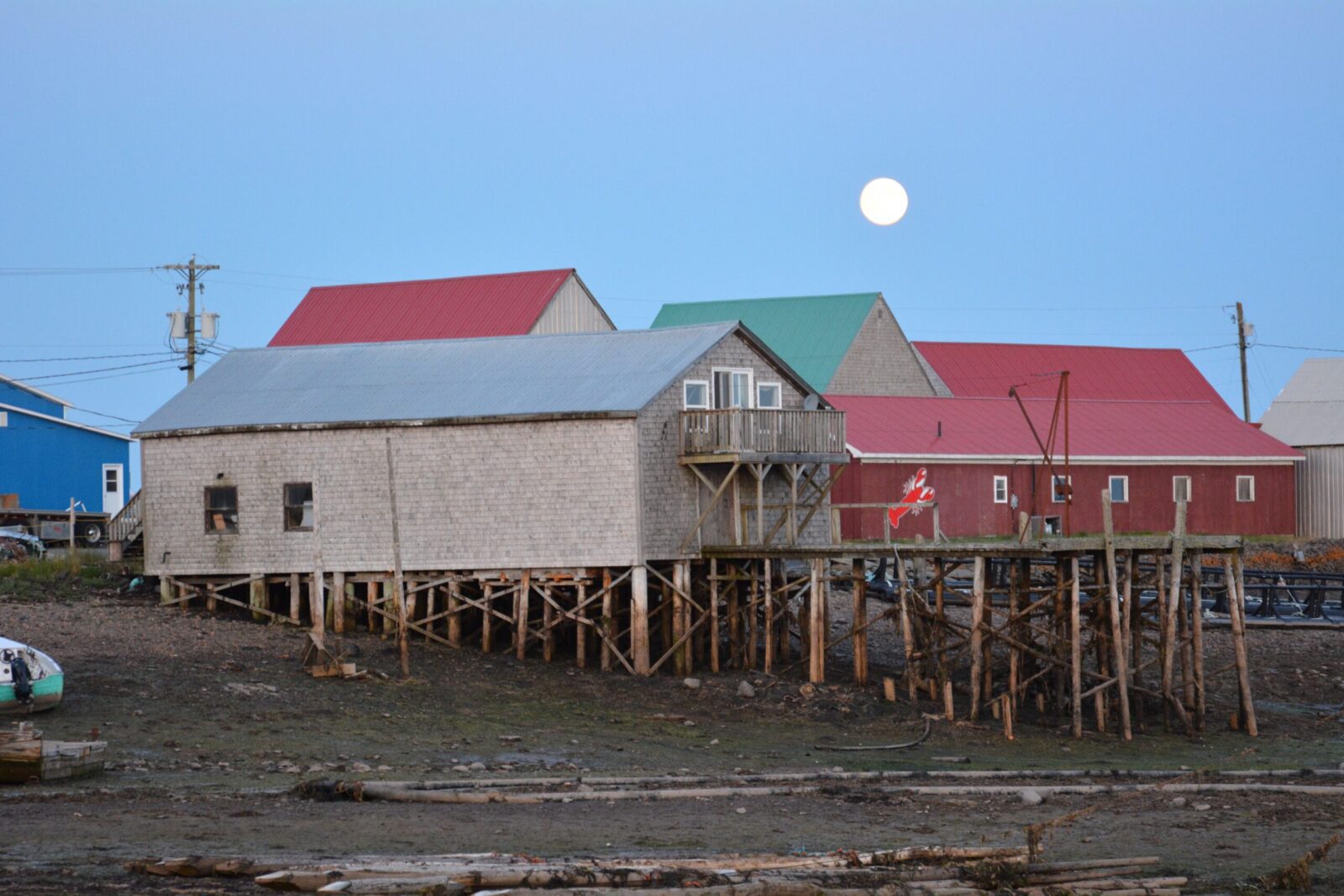 A full moon rises over a group of houses on the shore.