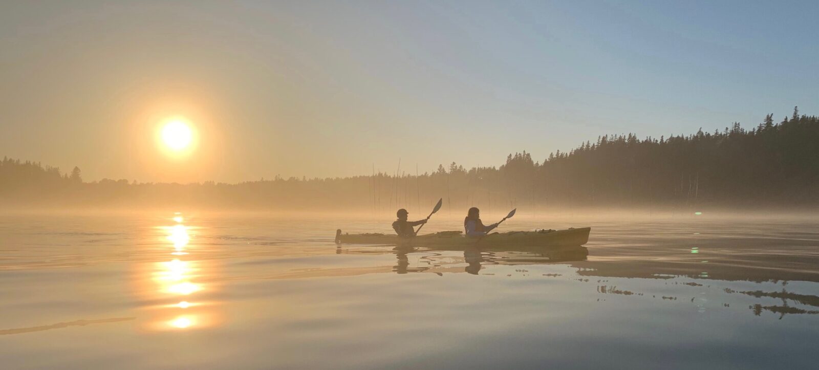 Two people paddling a canoe on a lake at sunrise.