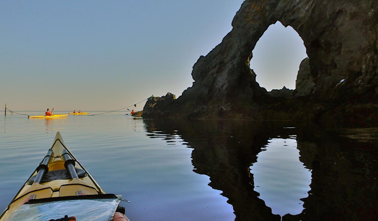 A kayaker is paddling in the water near a rock formation.
