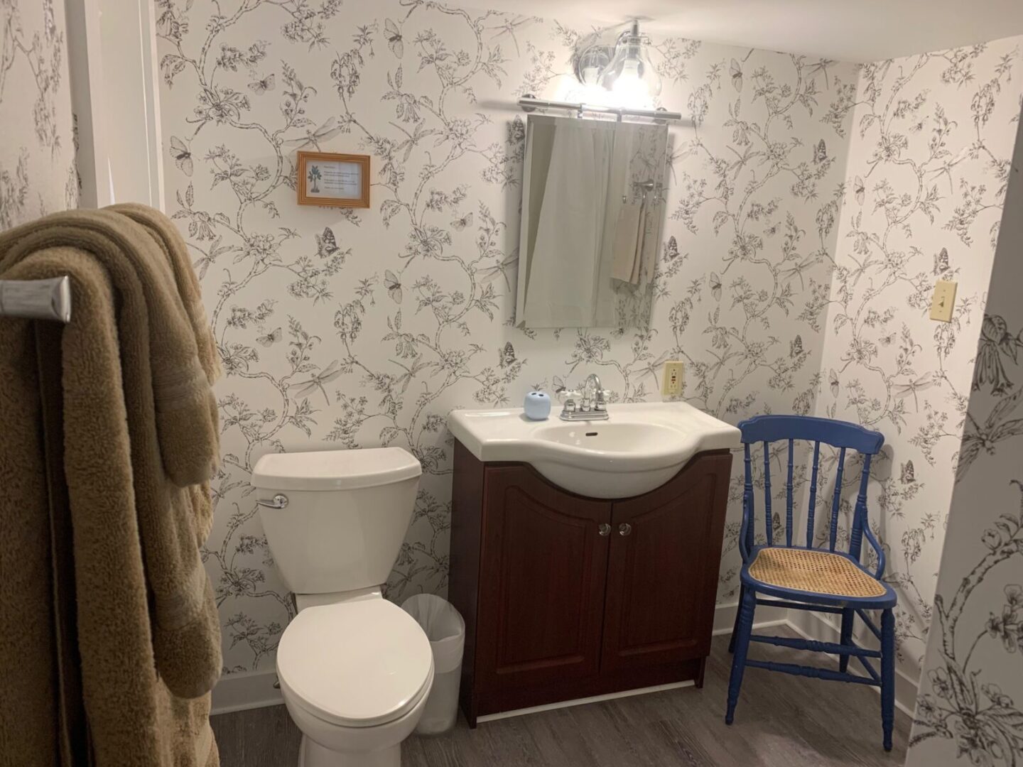 A bathroom with floral wallpaper and a blue chair.