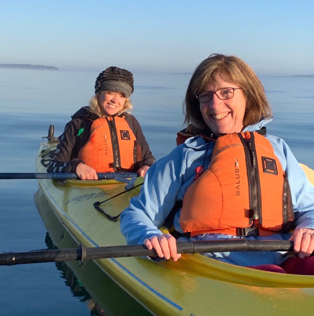 Two women in yellow kayaks smiling at the camera.
