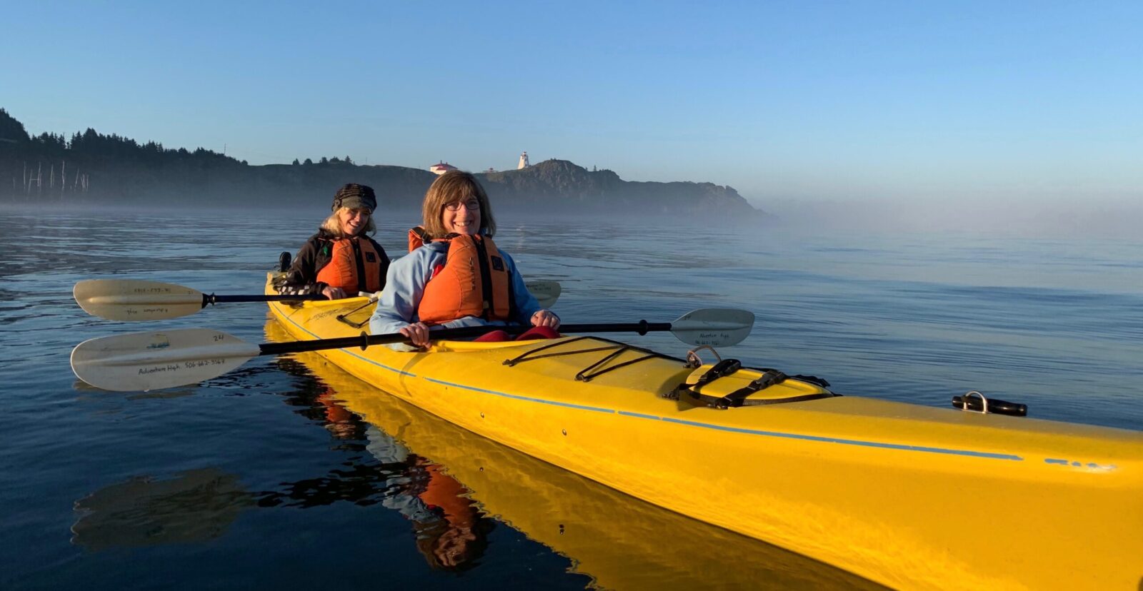 Two people paddling in a yellow kayak on the water.