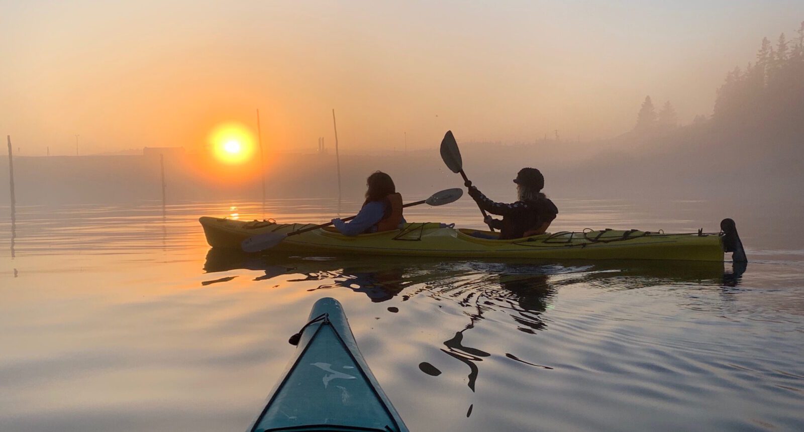 Two people paddling kayaks on a foggy morning.