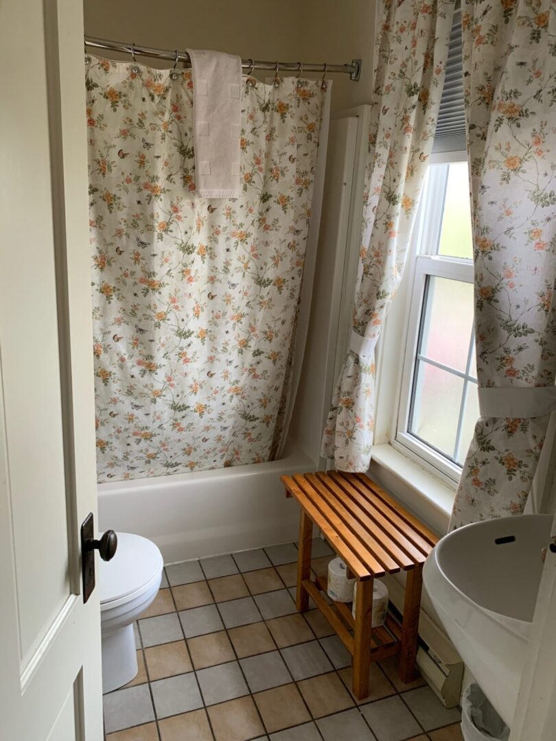A bathroom with a floral shower curtain and a wooden bench.