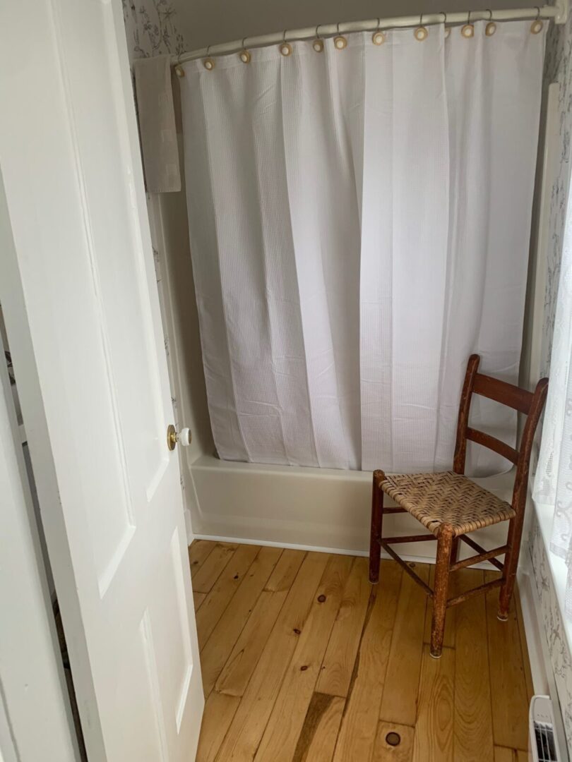 A bathroom with a white shower curtain and a wooden chair.