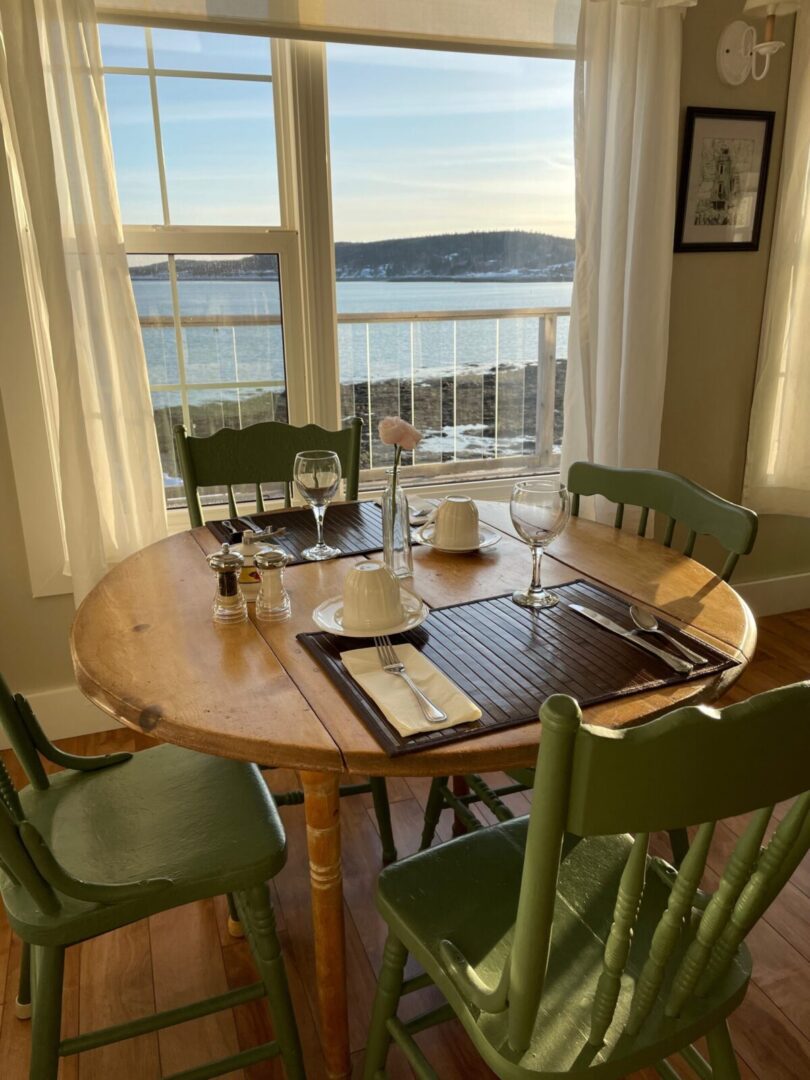 A table with green chairs and a view of the ocean.