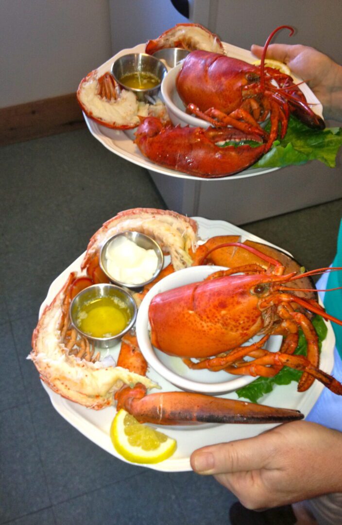 A person holding two plates with lobsters on them.