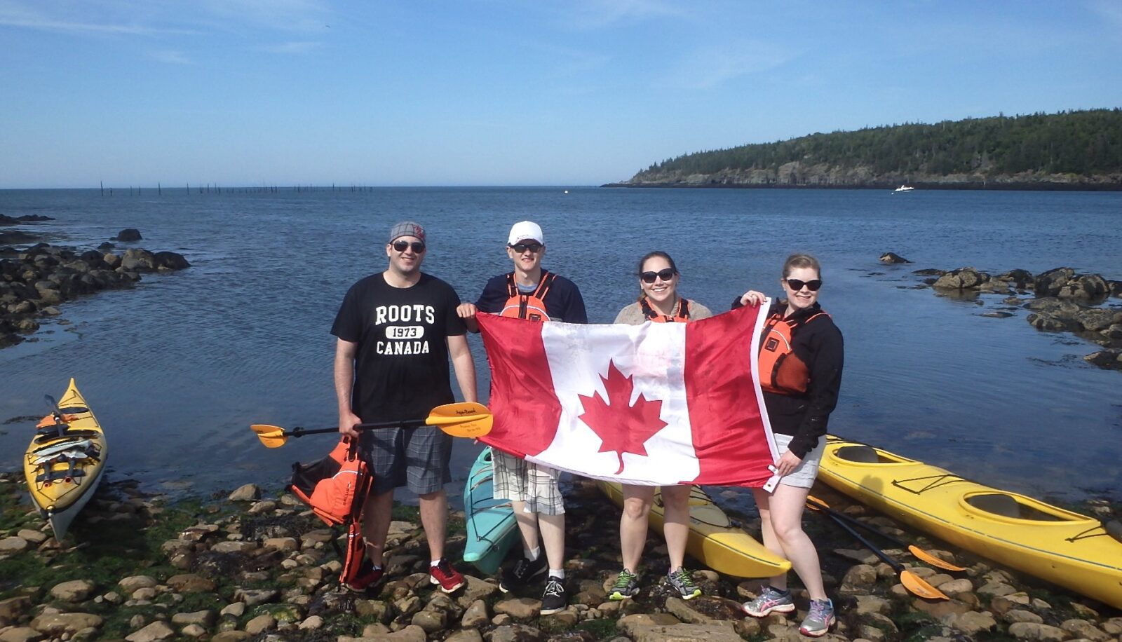 A group of people holding a canadian flag in front of a body of water.