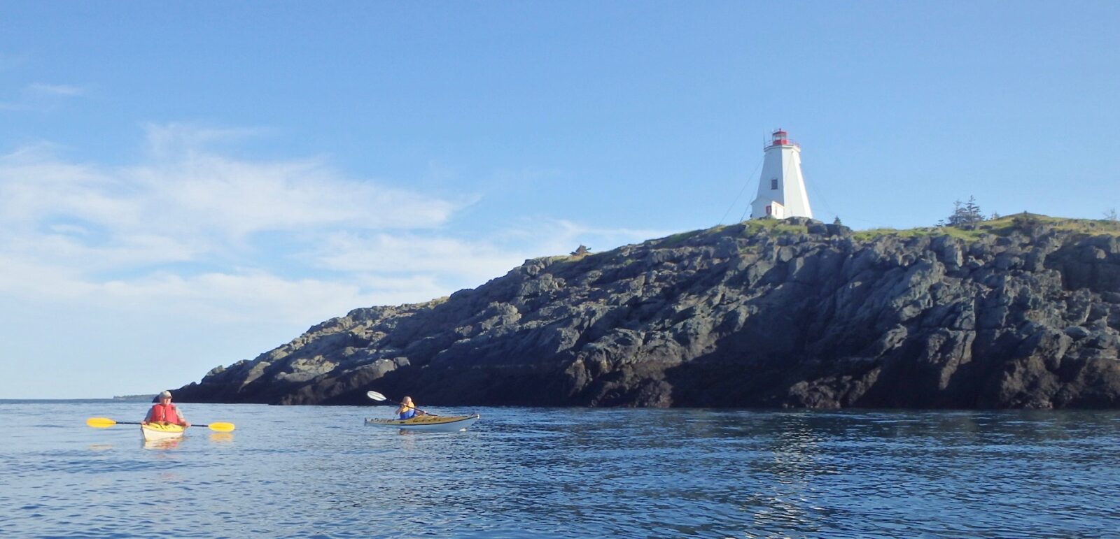 Two people paddling kayaks in the water near a lighthouse.