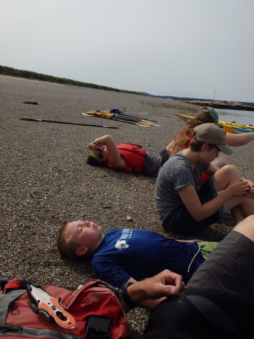 A group of people laying on the ground near a body of water.