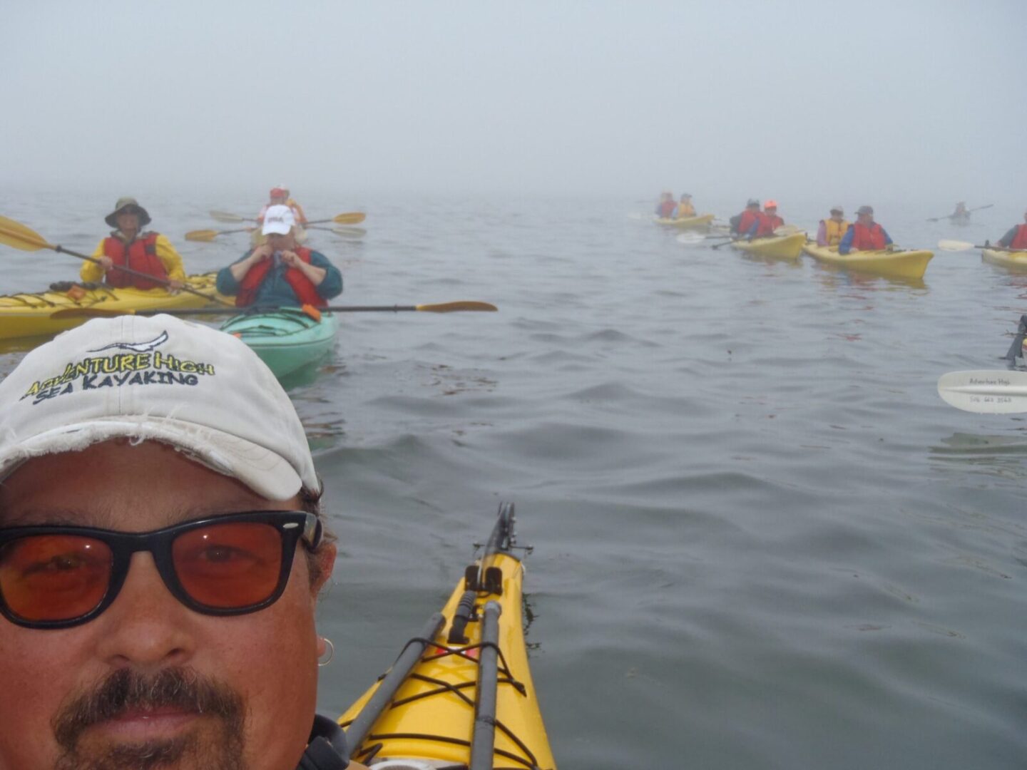 A man in a hat and sunglasses kayaking in the fog.