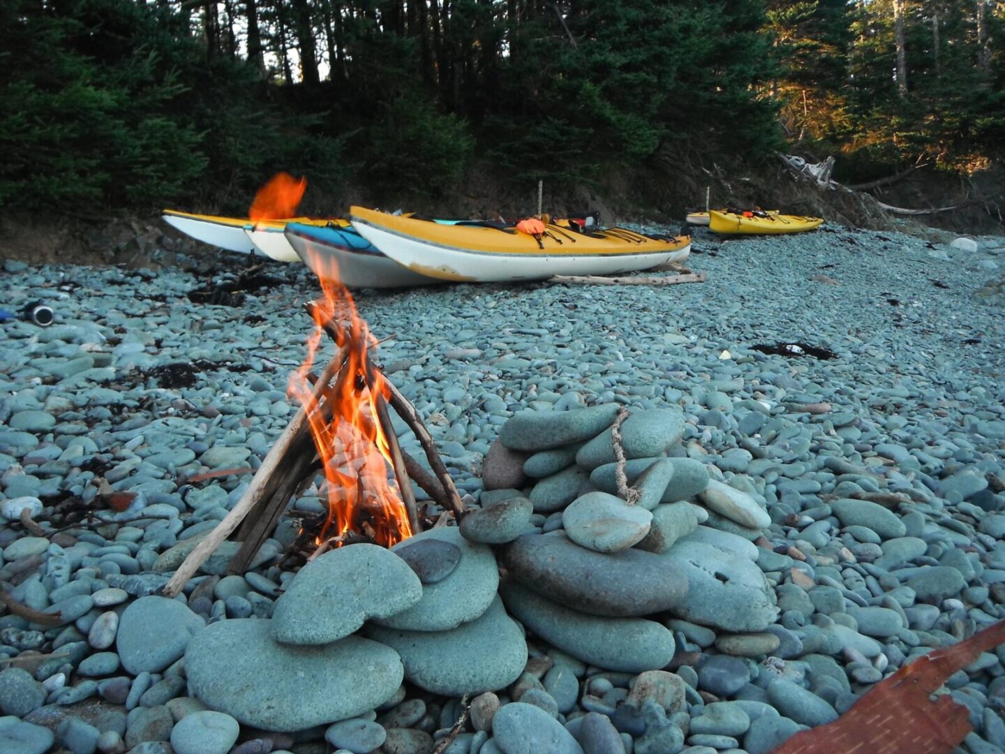 A campfire on a beach with kayaks in the background.
