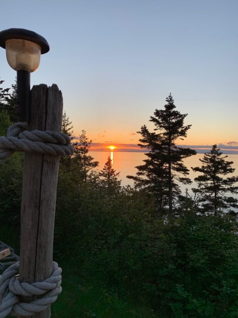 The sun is setting over a wooden post with a lamp on it.