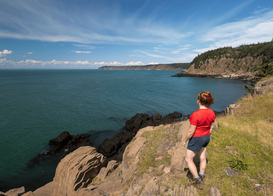 A woman is standing on a rocky cliff overlooking the ocean.