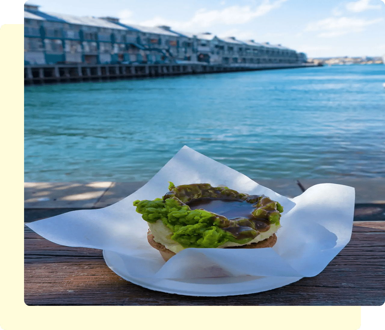 Avocado bagel by waterfront with buildings view.