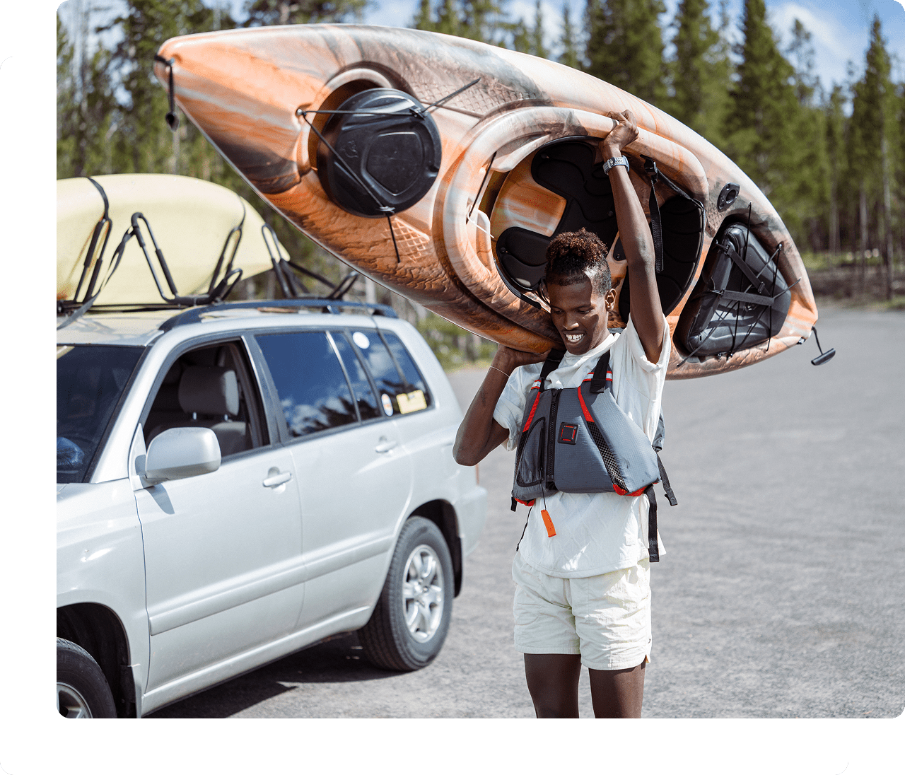 Person carrying kayak near parked car.