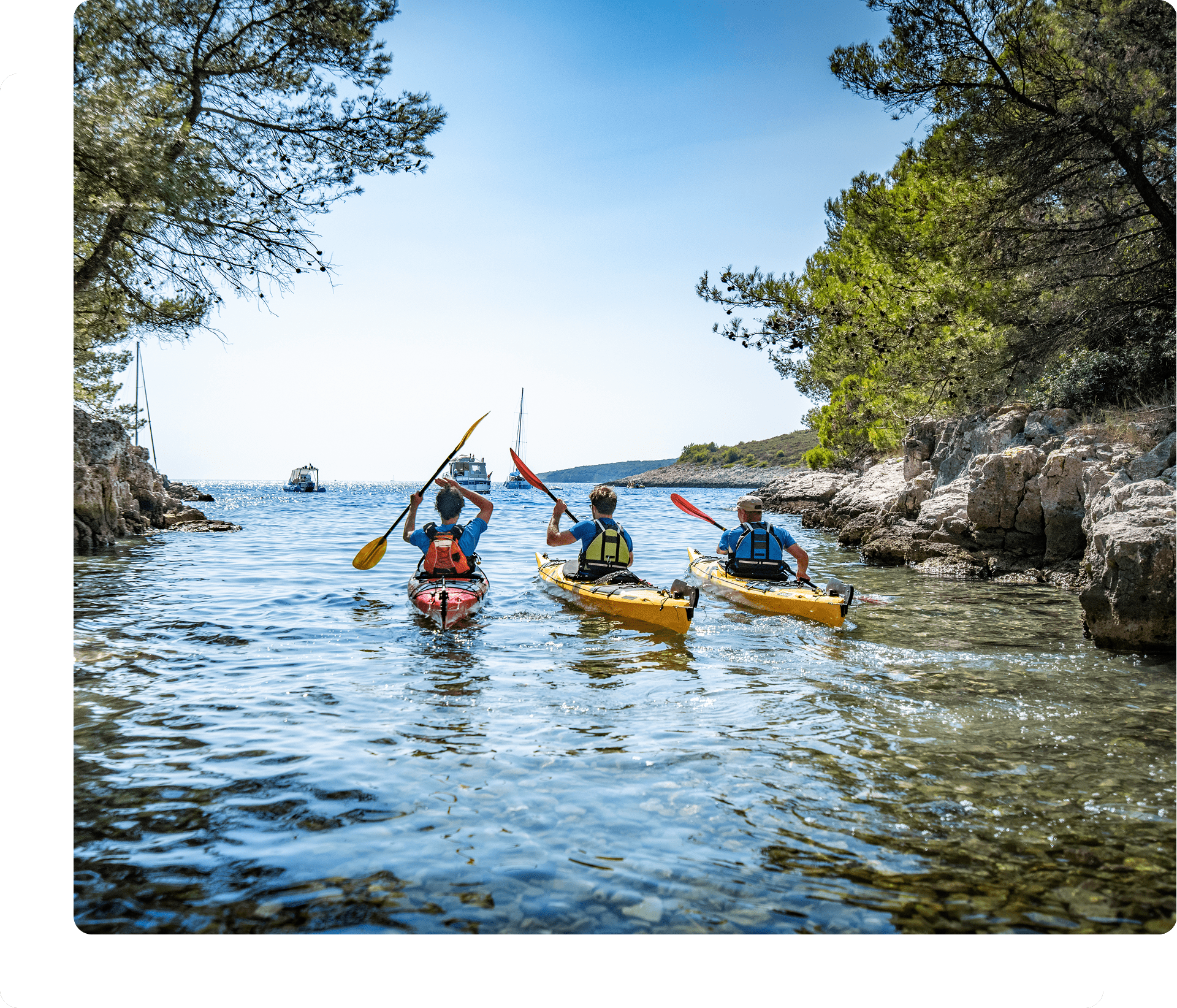 Three kayakers paddling on a scenic waterway.