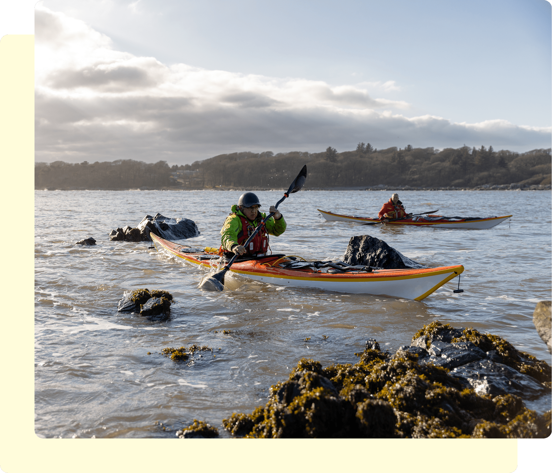 Kayakers navigating rocky waters under cloudy sky.