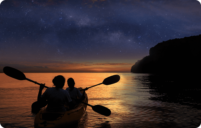 Two people kayaking at sunset under stars.