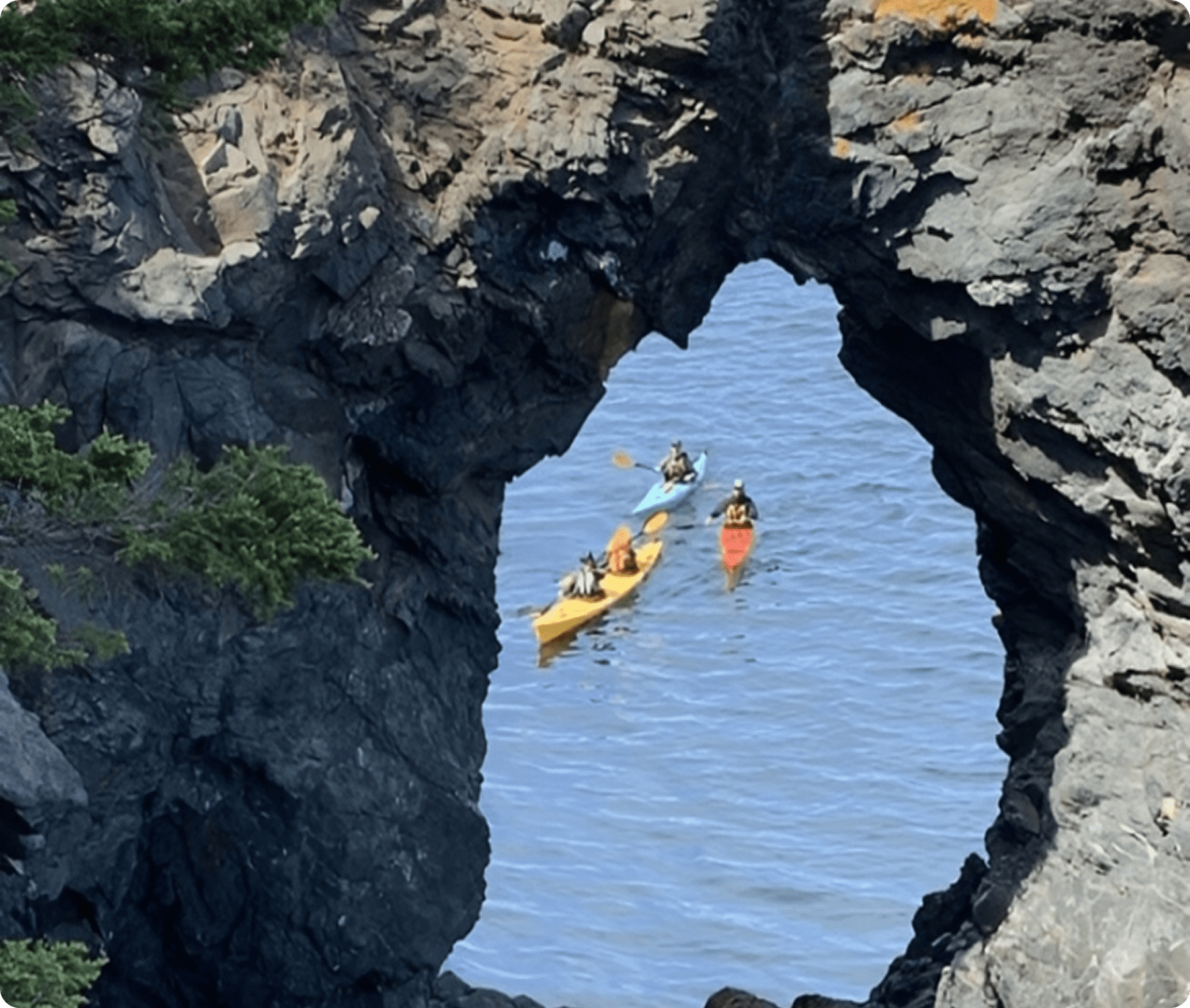 Kayakers passing through rocky sea arch.