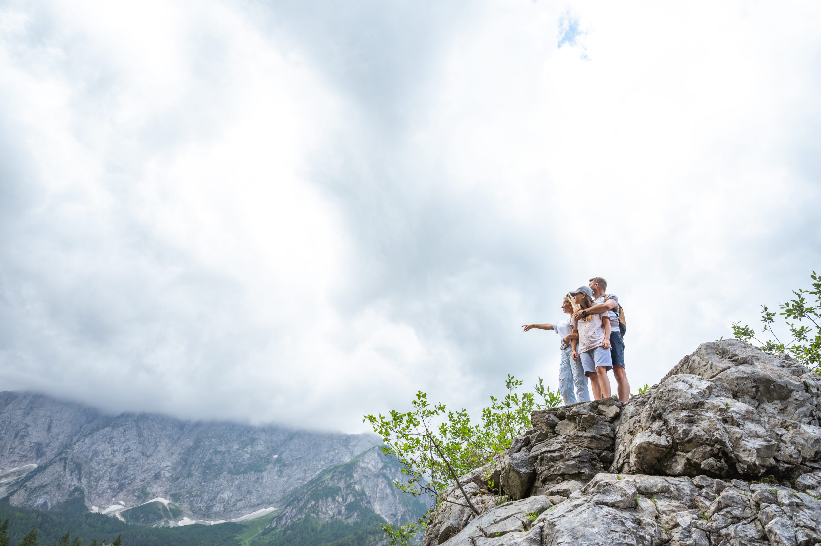 Family standing on rocky mountain, pointing skyward.