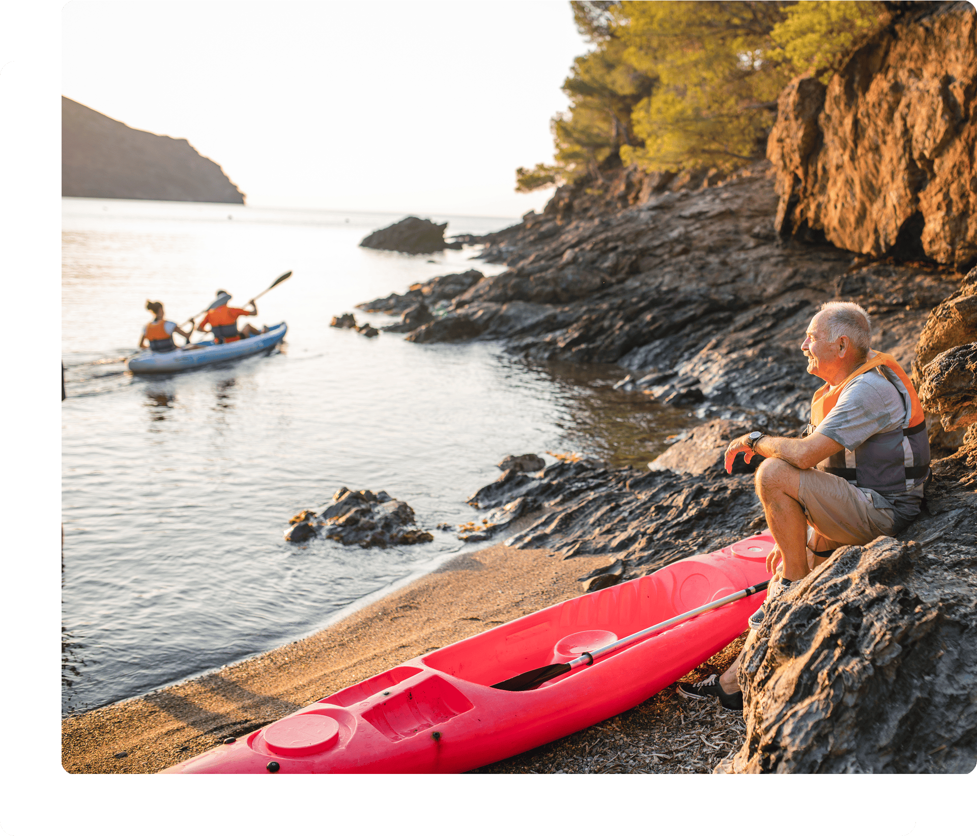 Man sitting by kayak on rocky shore.