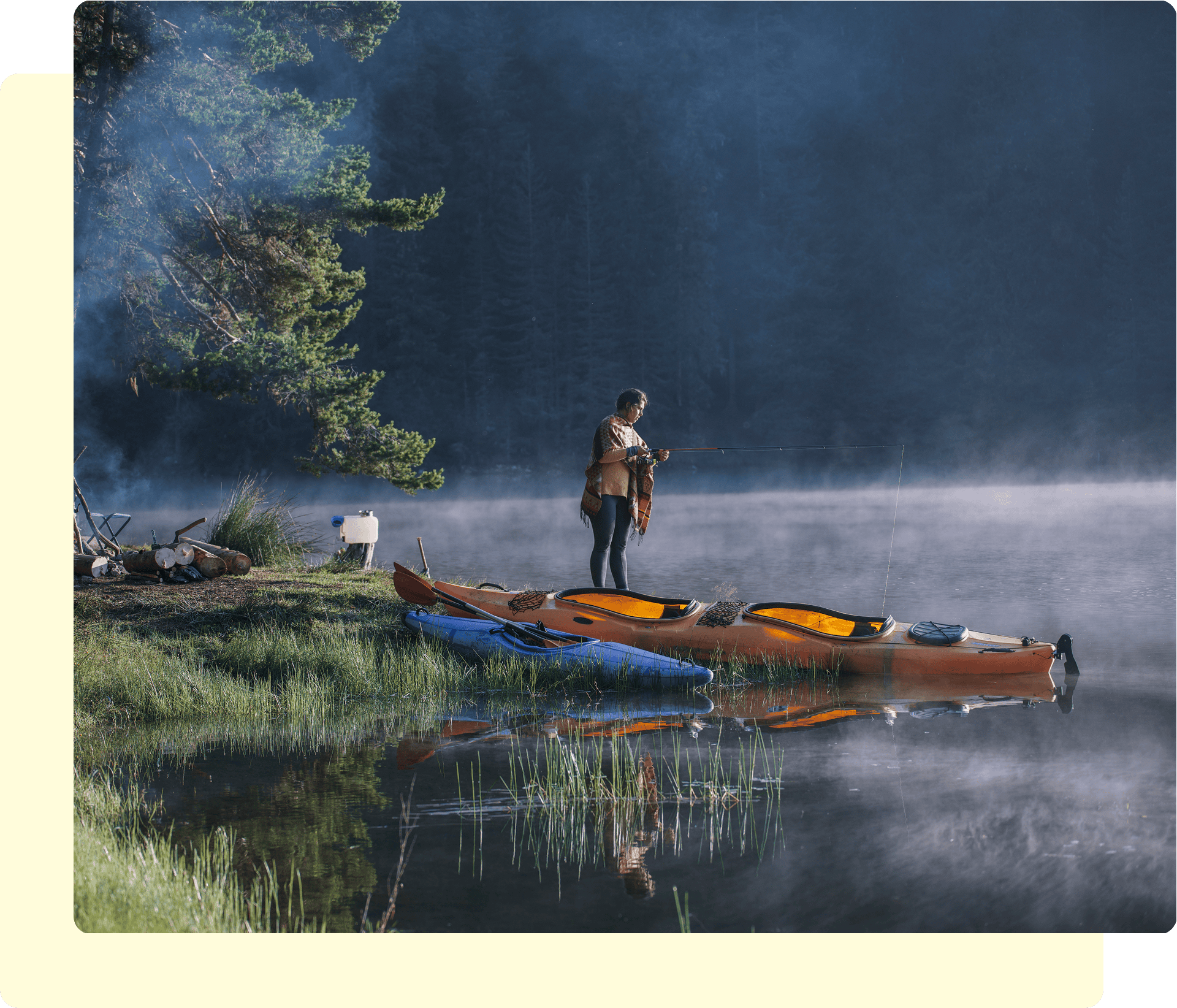 Person fishing beside kayaks on foggy lake.