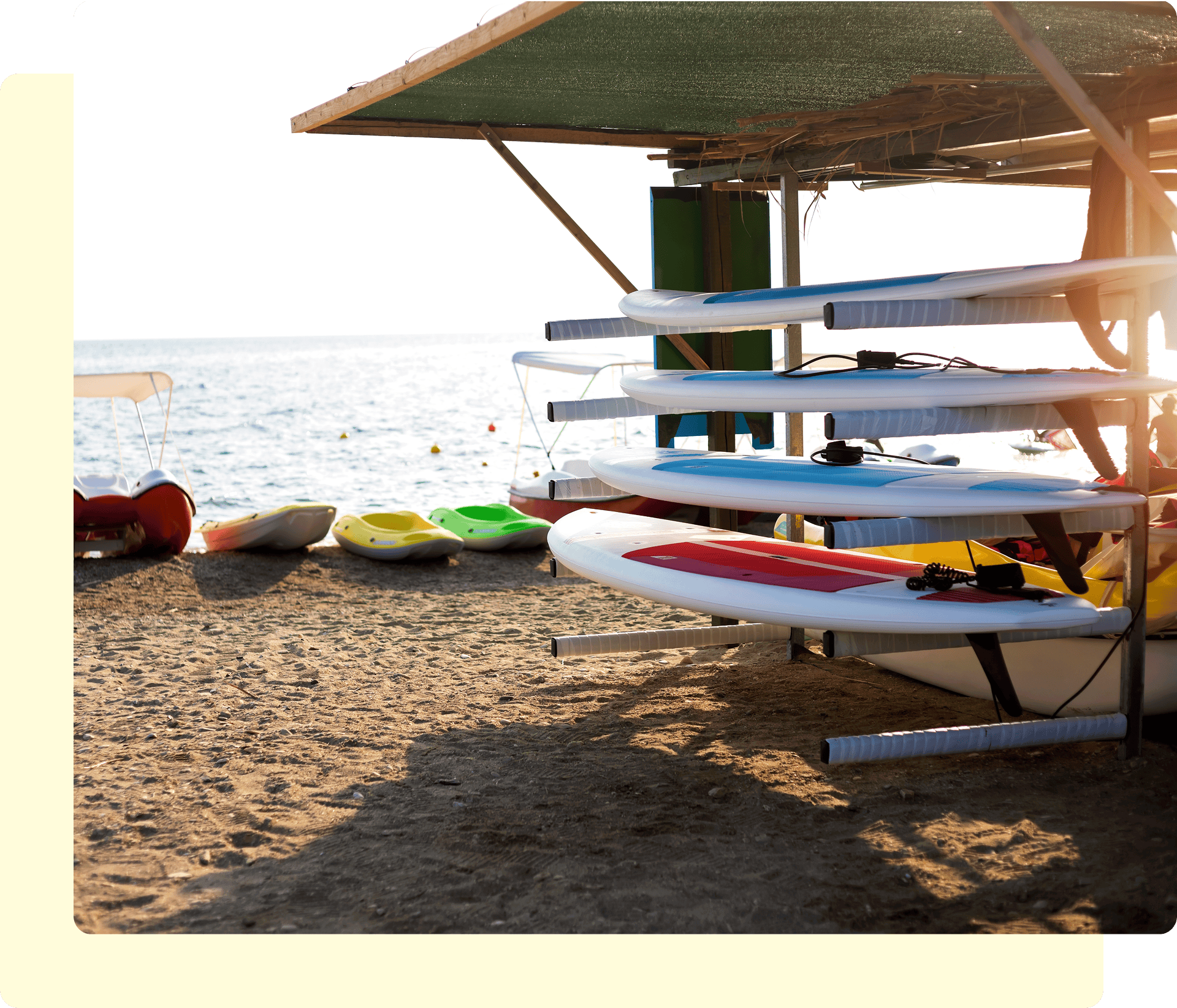 Stored surfboards and kayaks on sandy beach.