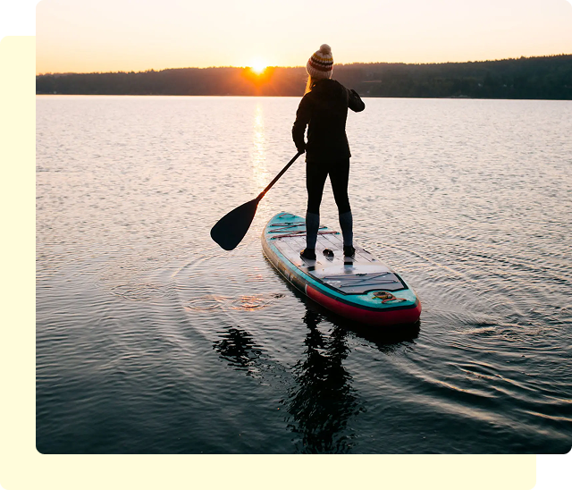 Person paddleboarding on a lake at sunset.
