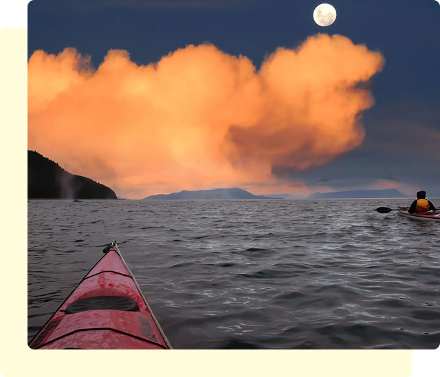 Kayakers under moonlit sky with orange clouds.