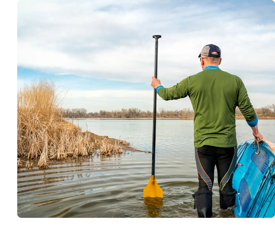 Man with paddleboard near lake, holding paddle.