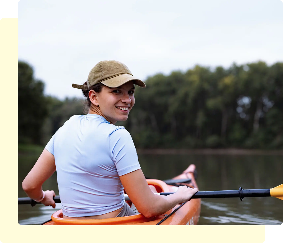 Person kayaking on a calm river, smiling.