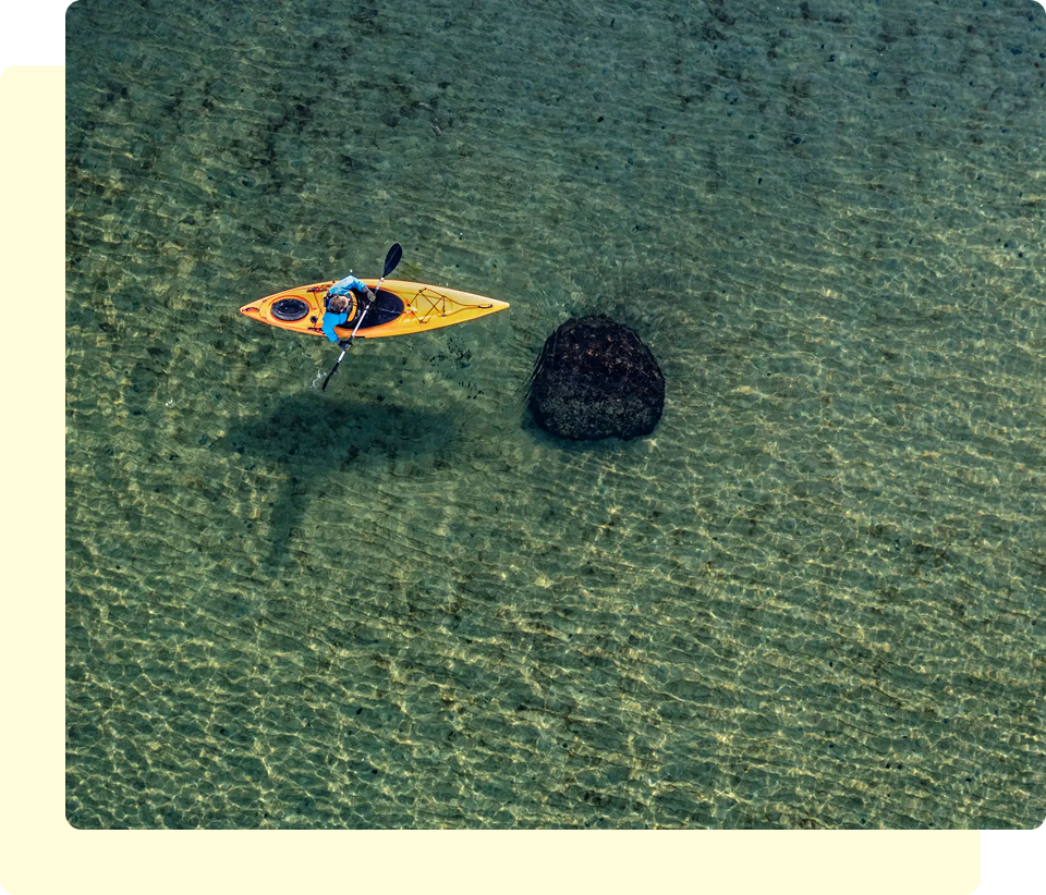 Kayaker paddling near a rock in water.