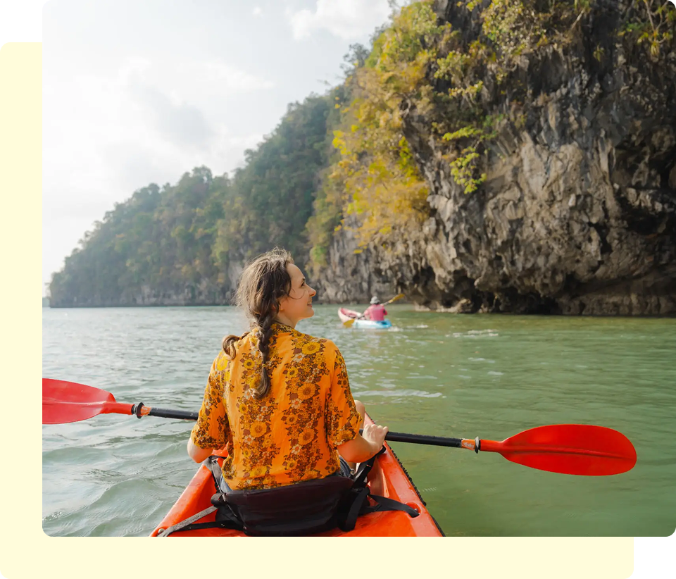 Woman kayaking near rocky coastline, sunny day.
