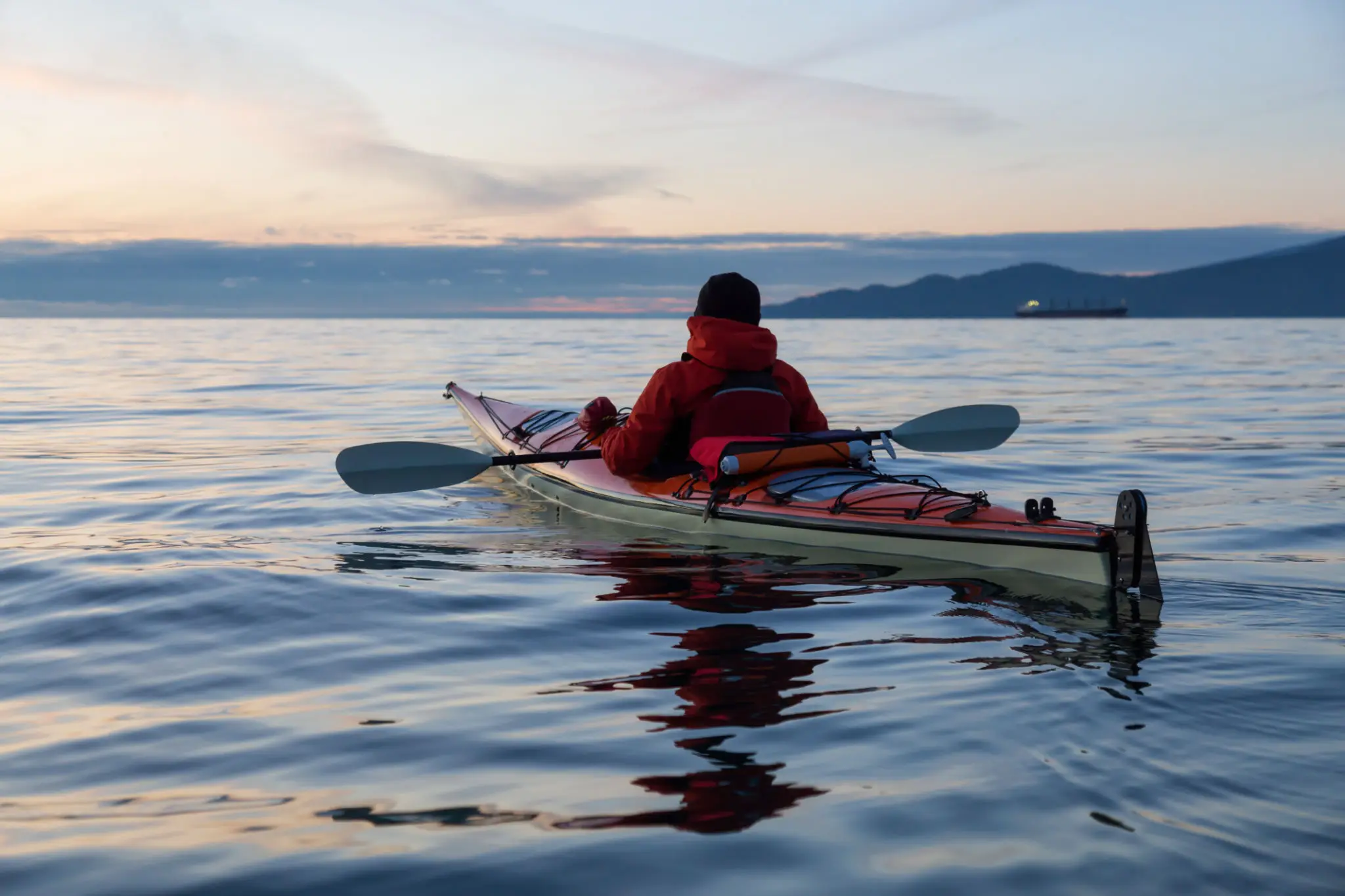 Person kayaking on calm water at sunset.