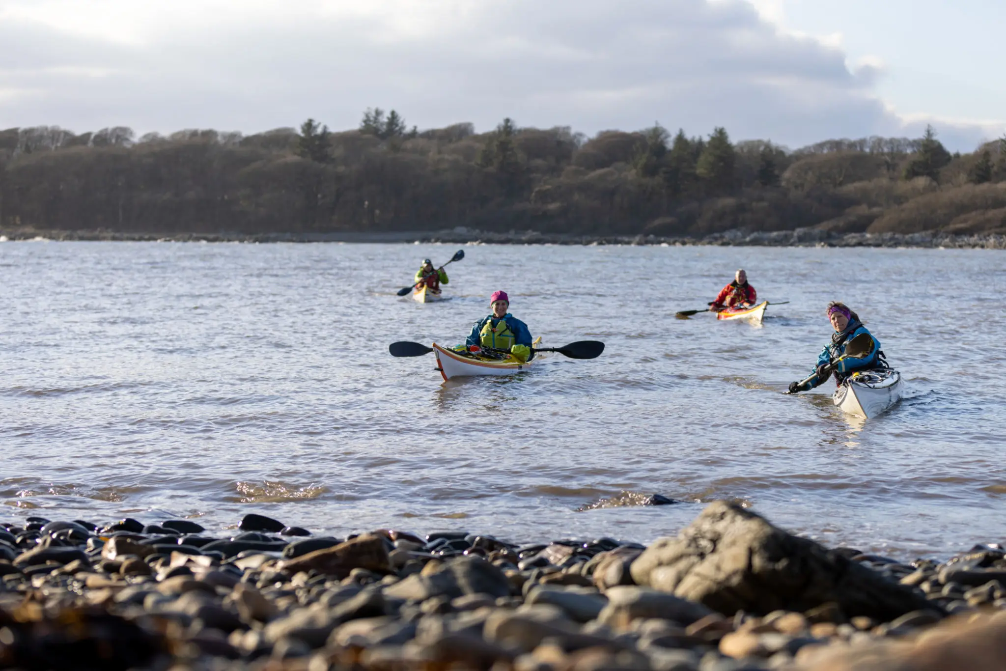 Kayakers paddling on a calm, rocky shoreline.