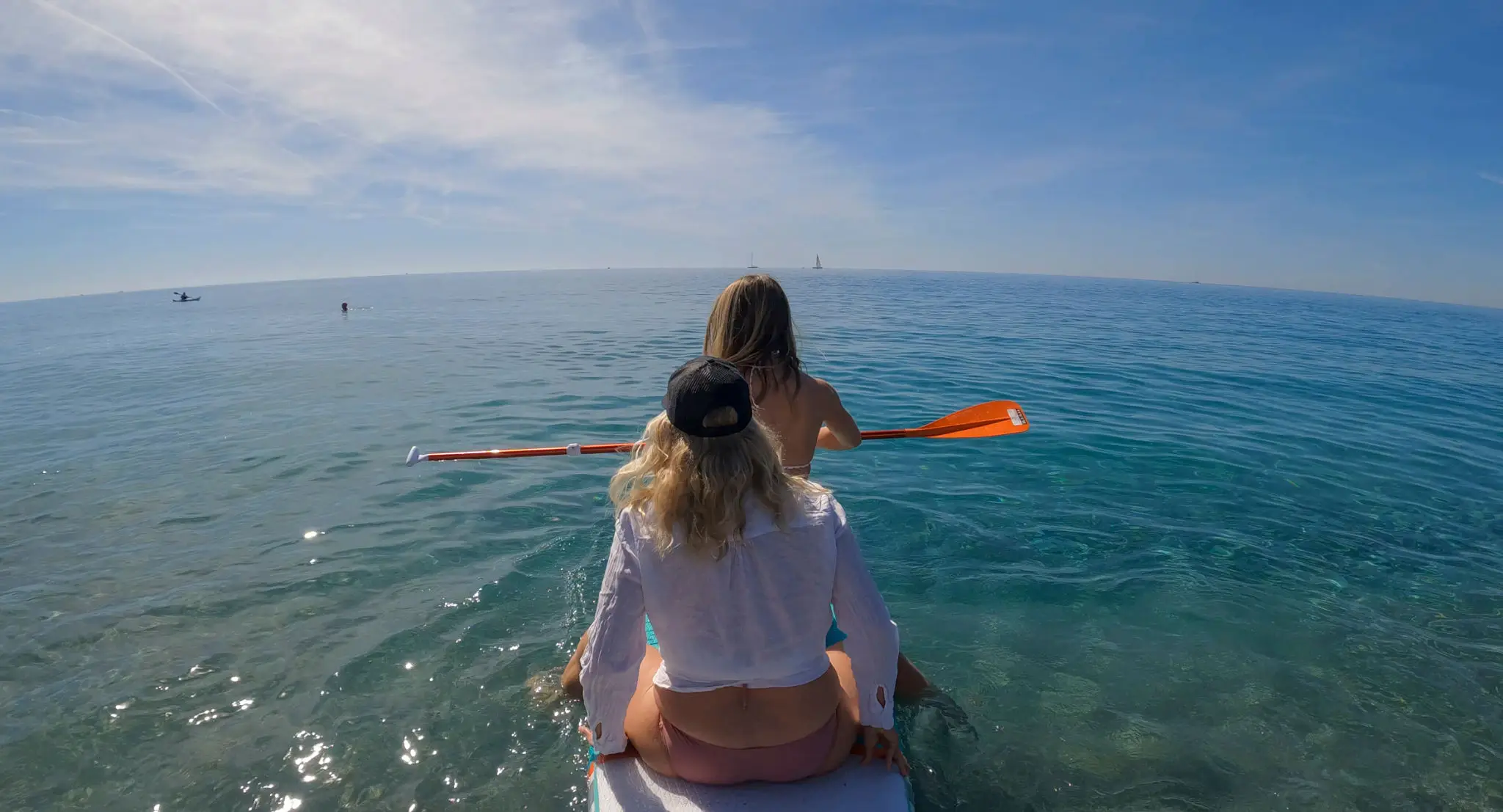 Two women kayaking on clear blue water.