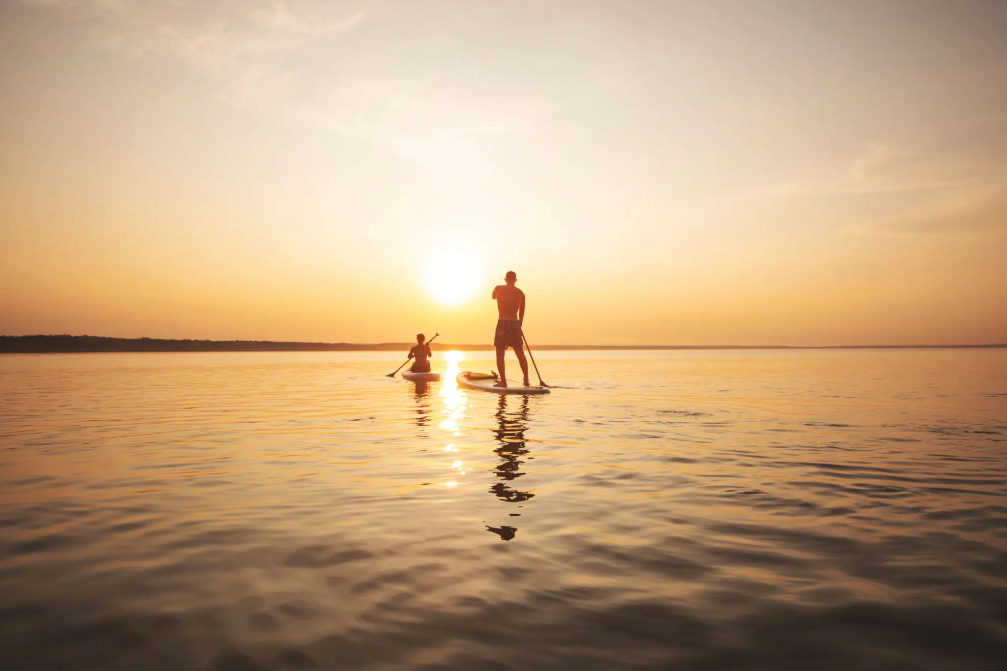 Two people paddleboarding at sunset.
