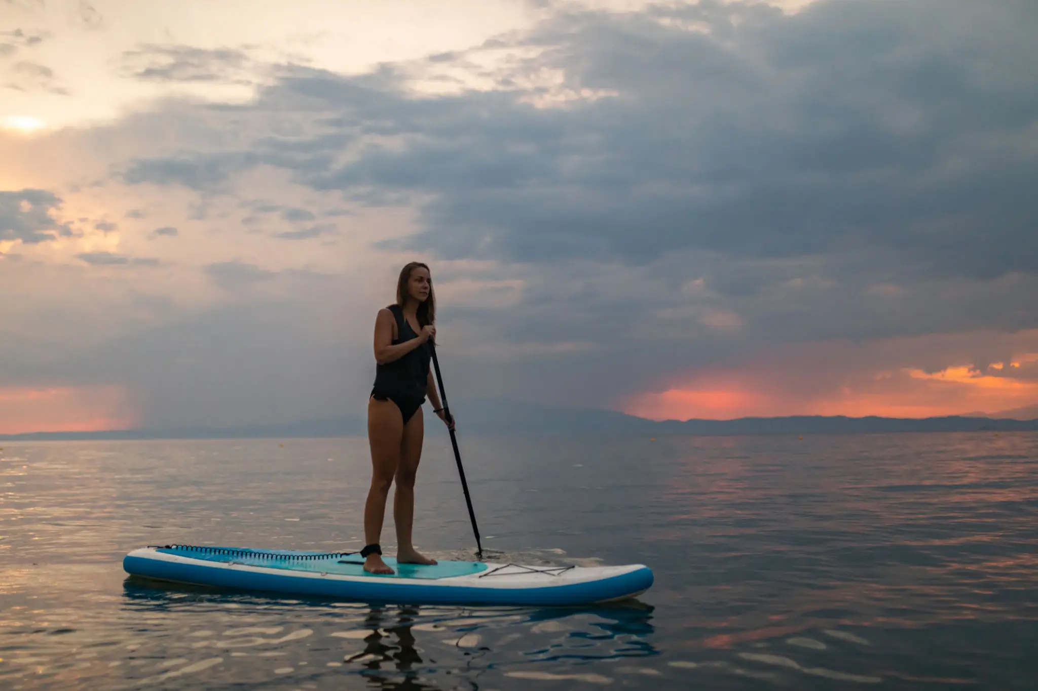 Woman paddleboarding during a colorful sunset.