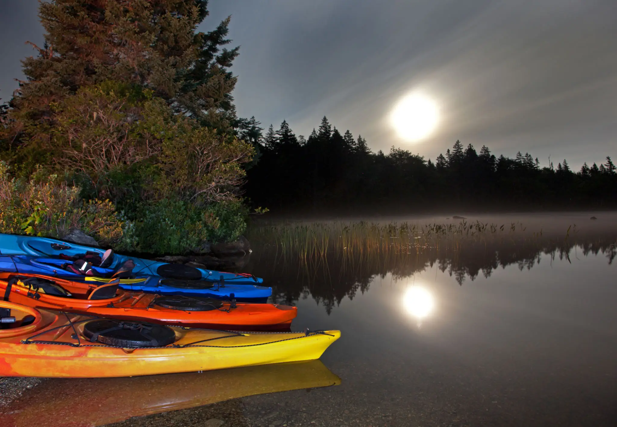 Colorful kayaks by a moonlit lake.
