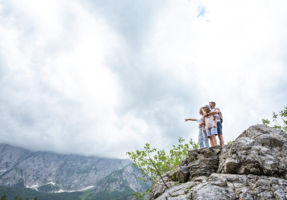 Family standing on rocky mountain, pointing skyward.