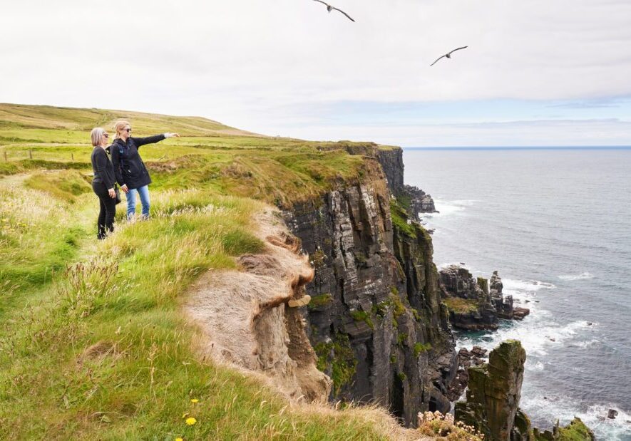 People standing on grassy cliff by ocean.