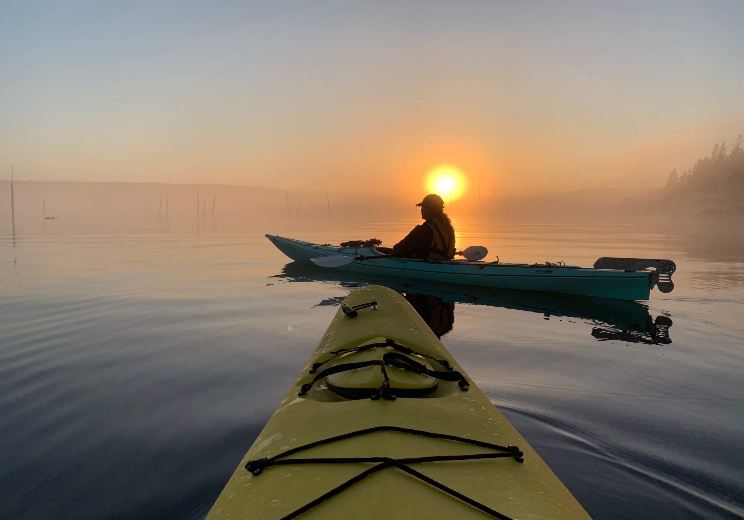 Kayakers on calm water during sunrise.