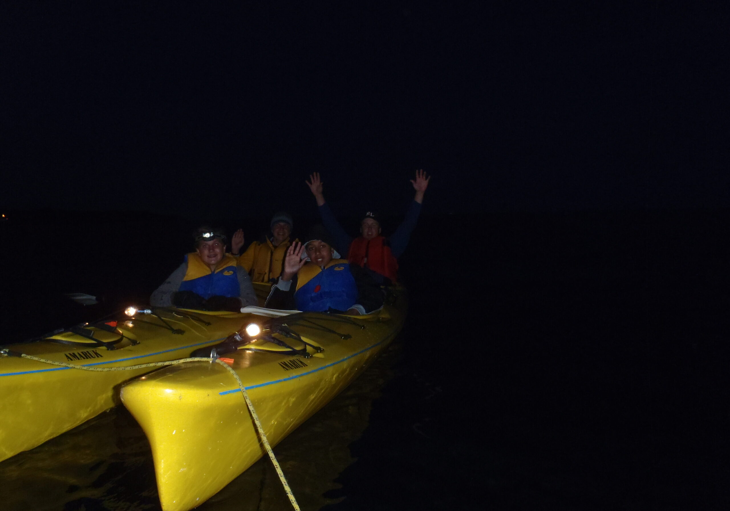 Group kayaking at night with raised arms.